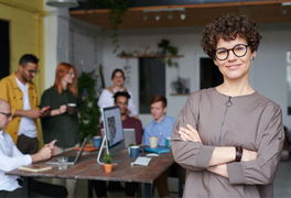 Frau steht im Vordergrund eines Tisches, an dem eine Gruppe von Menschen steht und sitzt